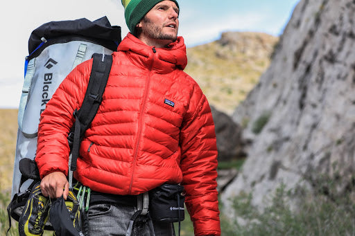 A man wearing a red coat in his 40’s hiking up the side of a mountain.