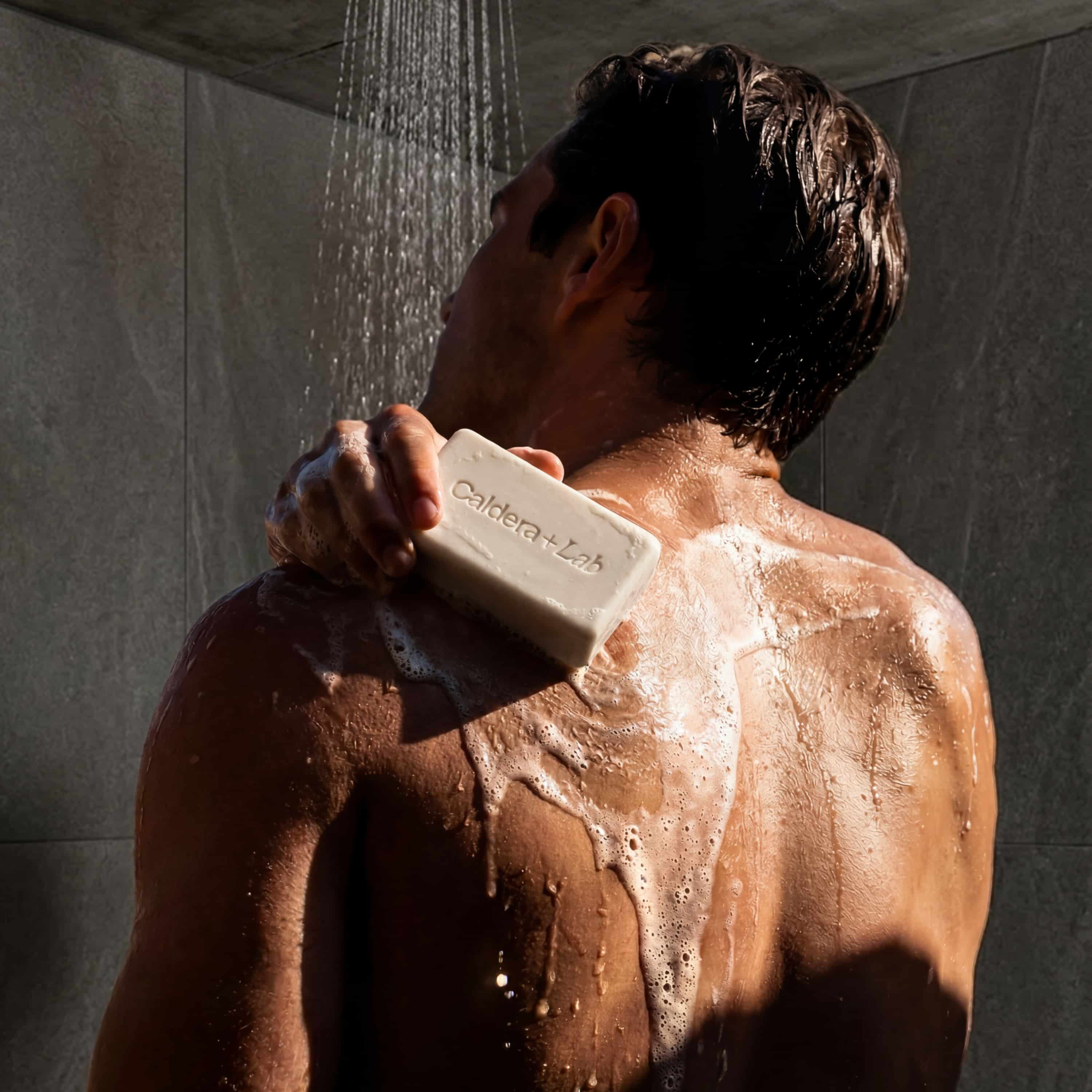 Man showering with a visible Caldera + Lab body bar and lather.