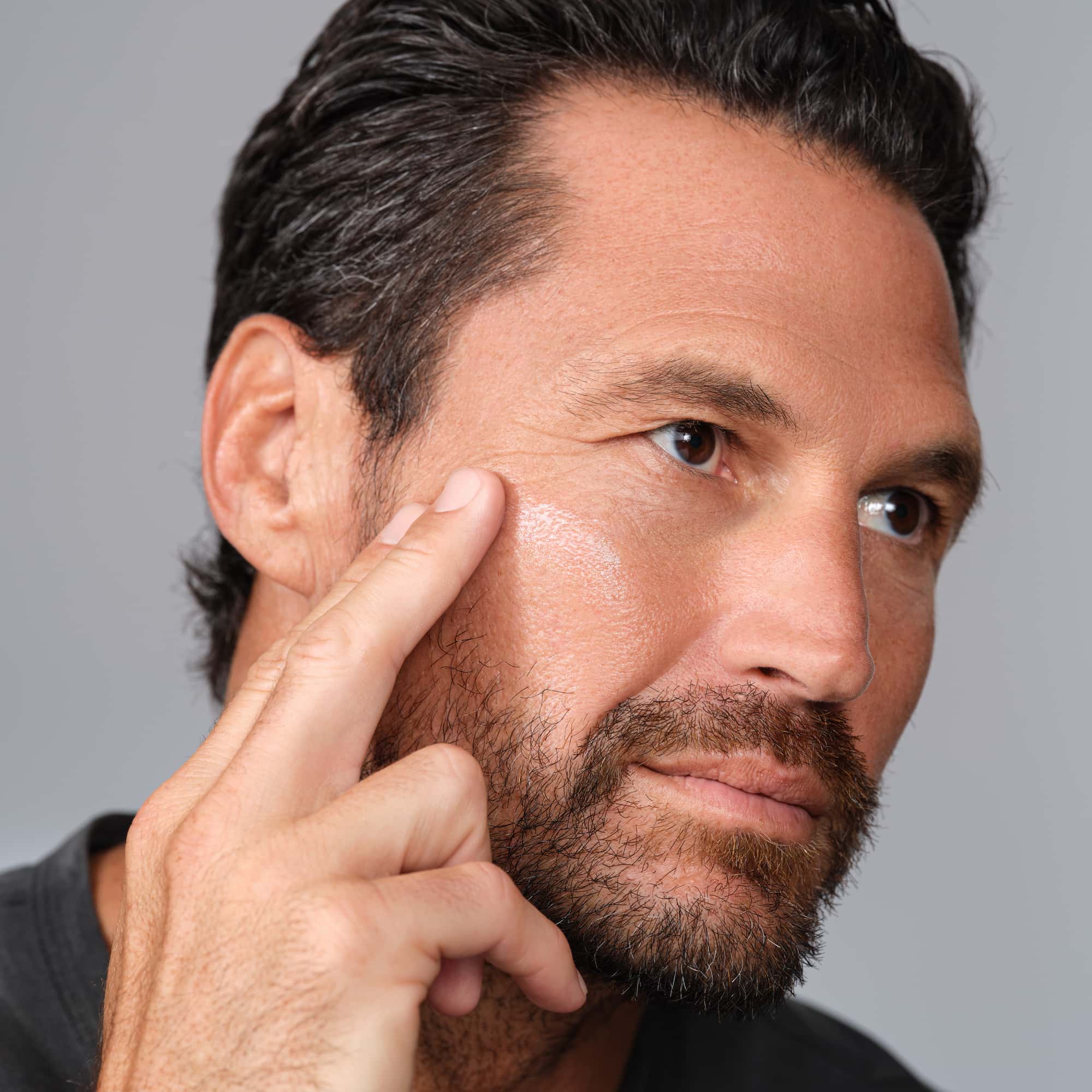 Man applying cream to his face against a gray background