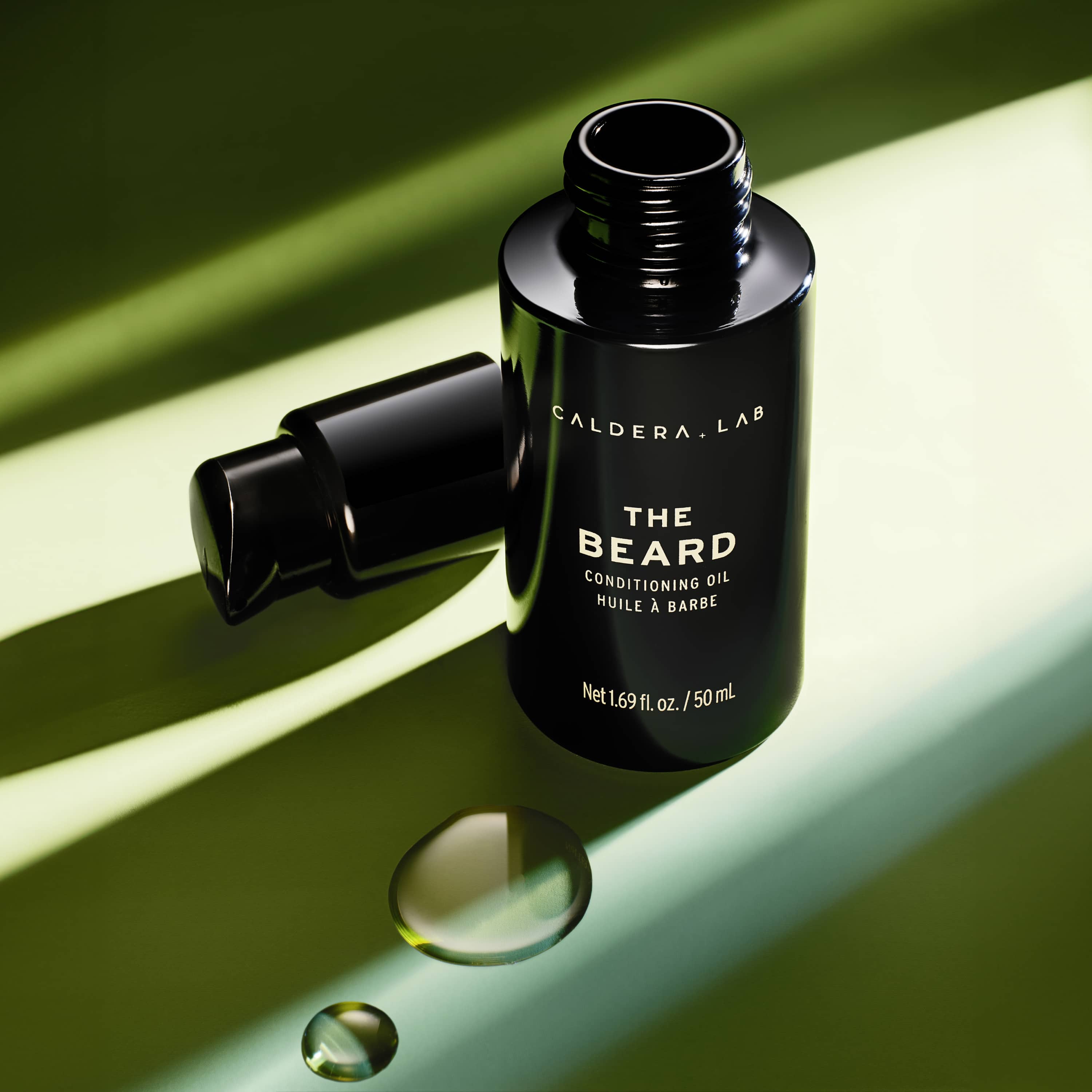 The Beard Conditioning oil by Caldera Lab, artistic photo with green background and some drops of oil in the foreground