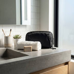 Bathroom counter with black toiletry bag, white soap, and plant on a tiled wall background